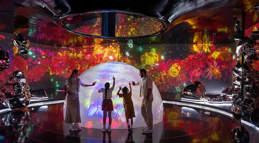 Visitors touch a glowing dome surrounded by colorful digital projections at Aya Universe Dubai.
